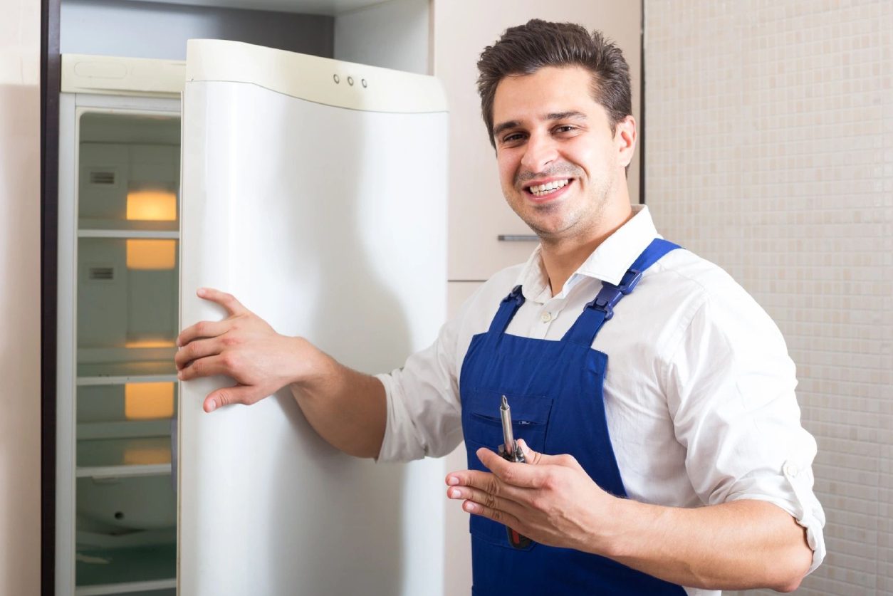 A man in an apron standing next to a refrigerator.